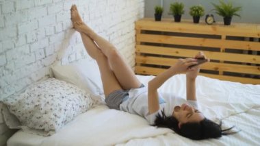 Genç kadın yatak ve onun smartphone kullanarak video sohbet yalan yan görünüm