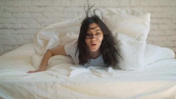 Young attractive woman lying in the bed, enjoying the morning at home. Girl looking at the camera and smiling. — Stock Video