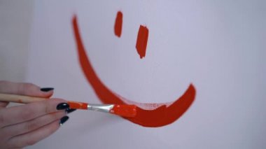 Mutlu bir surat, çocuksu tarzda bir kız sanatçı beyaz bir tuval üzerine bir gülümseme boyalı