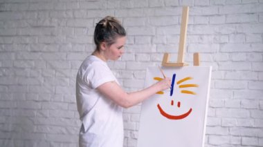 Mutlu bir surat, çocuksu tarzda bir kız sanatçı beyaz bir tuval üzerine bir gülümseme boyalı