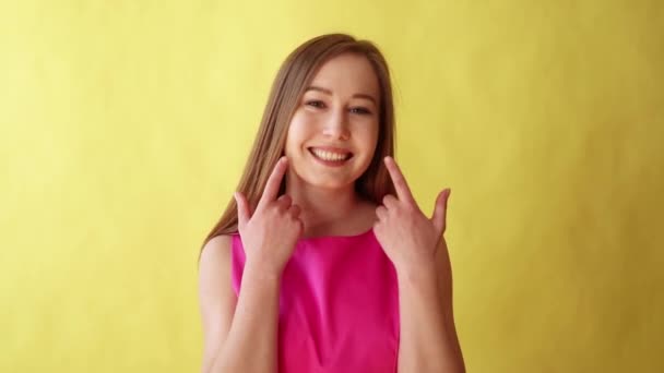 Primer plano de Mujer rubia joven sonríe grande a la cámara, revelando dientes blancos y perfectos sobre fondo amarillo — Vídeo de stock