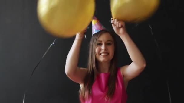 Χαριτωμένο μελαχρινή κρατώντας χρυσό μπαλόνια σε μαύρο φόντο. — Αρχείο Βίντεο