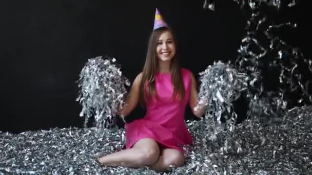La joven feliz en el vestido rosado celebra Nuevo año o el cumpleaños sobre el fondo negro con el confeti — Vídeo de stock