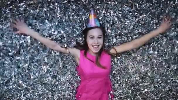 Счастливая молодая женщина в розовом платье празднует Новый год или день рождения на черном фоне с конфетти — стоковое видео