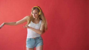 Hareket eden telefon tutarak ve kırmızı arka plan üzerinde kulaklık ile müzik dinleme genç oldukça beyaz kadın