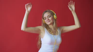 Hareket eden telefon tutarak ve kırmızı arka plan üzerinde kulaklık ile müzik dinleme genç oldukça beyaz kadın