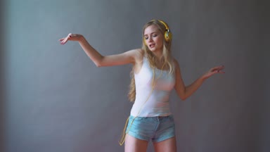 Gri bir arka plan üzerinde genç güzel kadın dans kulaklık telefon, müzik dinlemek