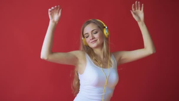 Joven mujer bastante caucásica sosteniendo el teléfono móvil y escuchando música con auriculares sobre fondo rojo — Vídeos de Stock