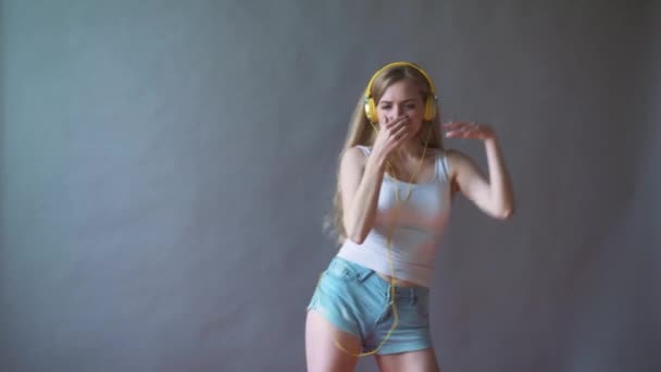 Νεαρή όμορφη γυναίκα σε ένα γκρίζο φόντο, να ακούτε μουσική στα ακουστικά στο τηλέφωνο, χορός — Αρχείο Βίντεο