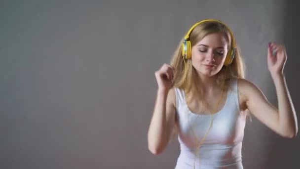 Молода красива жінка на сірому фоні, слухаючи музику в навушниках по телефону, танцює — стокове відео