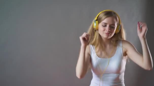 Joven hermosa mujer sobre un fondo gris, escuchando música en auriculares en el teléfono, bailando — Vídeos de Stock