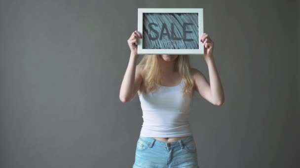 少女は、「販売」のサインを示しています。灰色の背景. — ストック動画