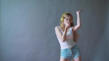 Gri bir arka plan üzerinde genç güzel kadın dans kulaklık telefon, müzik dinlemek