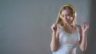 Gri bir arka plan üzerinde genç güzel kadın dans kulaklık telefon, müzik dinlemek