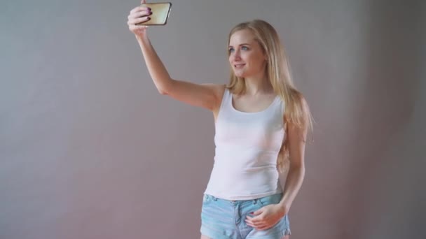 Beautiful girl with light makeup takes a selfie on a gray background. — Stock Video
