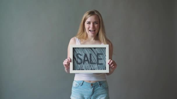 Flickan visar en skylt ”försäljning”. grå bakgrund. — Stockvideo