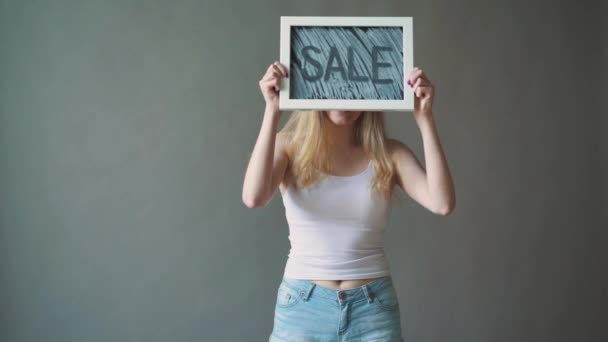 The girl shows a sign "SALE". gray background. — Stock Video