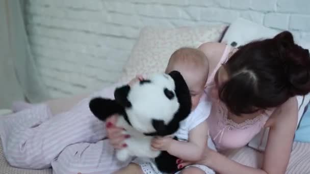Happy young mother and her girl with play on bed with toy Panda bear home smiling. — Stock Video
