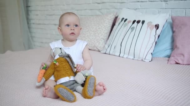Una hermosa niña está jugando con un conejo de juguete suave en la cama . — Vídeos de Stock