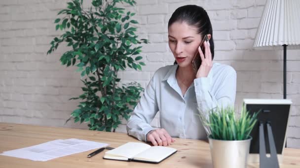 O femeie la o masă din birou vorbind la telefon . — Videoclip de stoc