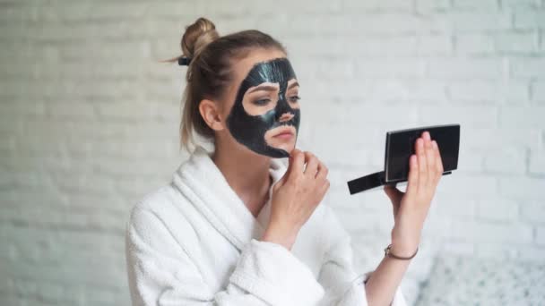 Mulher bonita remove máscara de limpeza do rosto no fundo de tijolo branco . — Vídeo de Stock
