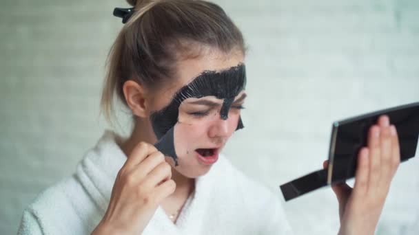 Mooie vrouw verwijdert reinigende masker uit gezicht op witte bakstenen achtergrond. — Stockvideo