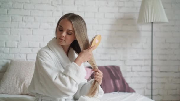 Mulher feliz em Bathrobe no quarto penteando belo cabelo longo . — Vídeo de Stock