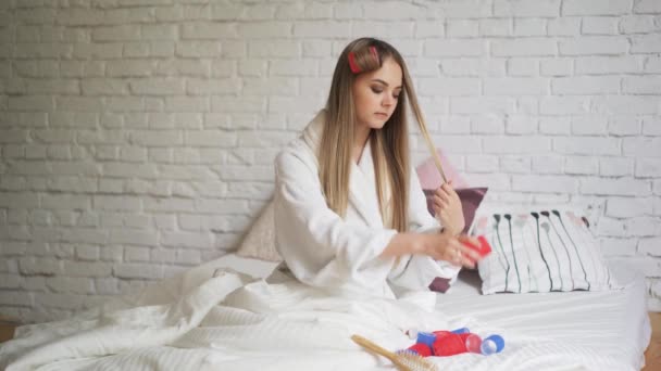 Bella ragazza seduta in camera da letto sul letto torce bigodini, bei capelli sani — Video Stock