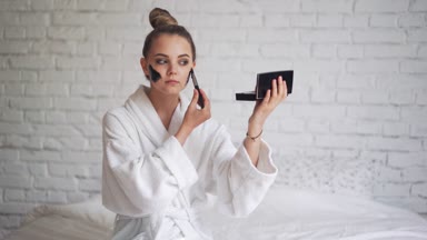 Kafasında havluyla gülen genç bir kız yüzüne siyah bir maske takıyor.