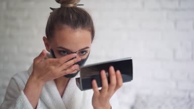 Kafasında havluyla gülen genç bir kız yüzüne siyah bir maske takıyor.