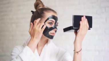 Kafasında havluyla gülen genç bir kız yüzüne siyah bir maske takıyor.