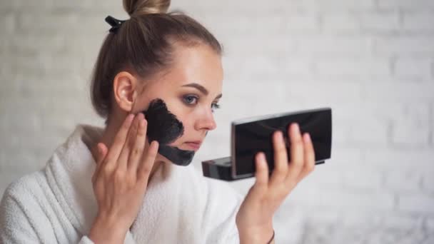 Lachende junge Mädchen mit einem Handtuch auf dem Kopf legt eine schwarze Maske auf ihr Gesicht, Day Spa — Stockvideo