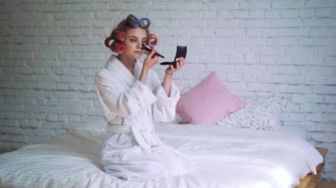 Dışarı çıkmak için hazır Başlarken saç silindirler giymiş ruj koyarak makyaj genç kadın.