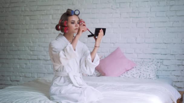 Makeup young woman putting lipstick wearing hair rollers getting ready for going out. — Stock Video