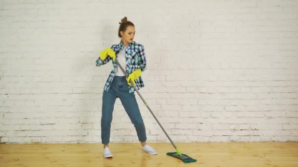 Hermosa joven mujer está bailando y sonriendo mientras limpia el piso en casa usando una fregona — Vídeos de Stock