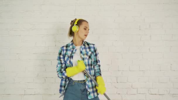 A young woman with headphones and a MOP is ready for home cleaning. Dancing and singing to good music — Stock Video