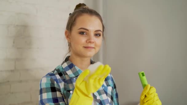 Netheid, hygiëne, huishoudelijke taken, plichten en huishoudelijk werk concept - mooi blond meisje waait schuim uit de hand. Gelukkige vrouw in uniform en handschoenen houdt reinigingsmiddel spray en spons met schuim. — Stockvideo