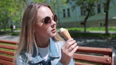 Genç kız elleri, dondurma ile bir bankta oturan beyaz t-shirt, kot, kot pantolon ve güneş gözlüğü giyiyor