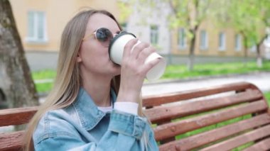 İçkiler ve insanlar konsepti - mutlu genç kadın ya da genç kız şehir bankında oturmuş kağıt bardaktan kahve içiyor.