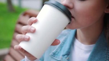 İçkiler ve insanlar konsepti - mutlu genç kadın ya da genç kız şehir bankında oturmuş kağıt bardaktan kahve içiyor.