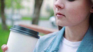 İçkiler ve insanlar konsepti - mutlu genç kadın ya da genç kız şehir bankında oturmuş kağıt bardaktan kahve içiyor.