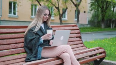 Bir bankta oturan ve bir yaz parkta okuma sırasında bir fincan kahve içmek için genç bir öğrenci bir dizüstü bilgisayar ile