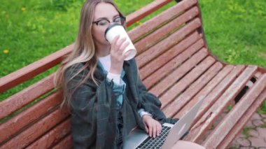 Bir bankta oturan ve bir yaz parkta okuma sırasında bir fincan kahve içmek için genç bir öğrenci bir dizüstü bilgisayar ile