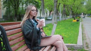 Bir bankta oturan ve bir yaz parkta okuma sırasında bir fincan kahve içmek için genç bir öğrenci bir dizüstü bilgisayar ile