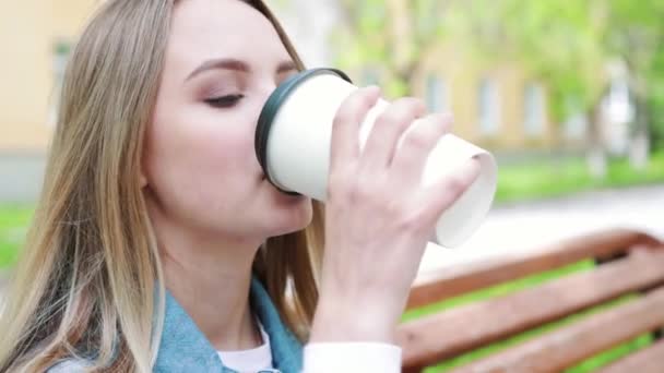 饮酒与人的概念- -快乐的年轻女性或少女坐在城市街头的长椅上，用纸杯喝咖啡 — 图库视频影像
