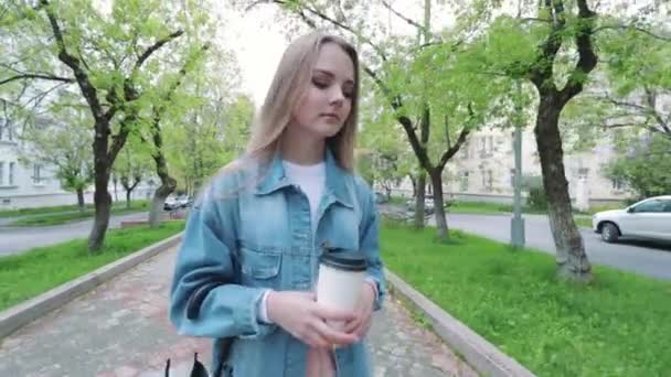 A young student with a laptop to drink a Cup of coffee while sitting on a bench and reading in a summer Park — Stock Video