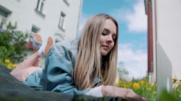 Meisje liggend in het gras, werken met een laptop. — Stockvideo