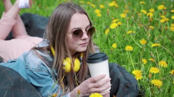 Όμορφη νεαρή γυναίκα απολαμβάνει πίνοντας καφέ και που βρίσκονται στο γρασίδι. Γυναίκα που πίνει καφέ. — Αρχείο Βίντεο