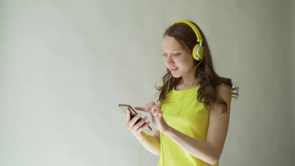 Hermosa morena sonriente escucha música usando auriculares en el estudio sobre fondo gris . — Vídeos de Stock