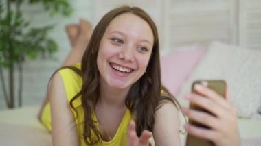 Yatak odası sabah yatakta yatarken hücre akıllı telefon mutlu gülümseyen güzel kız kullanan genç kadın